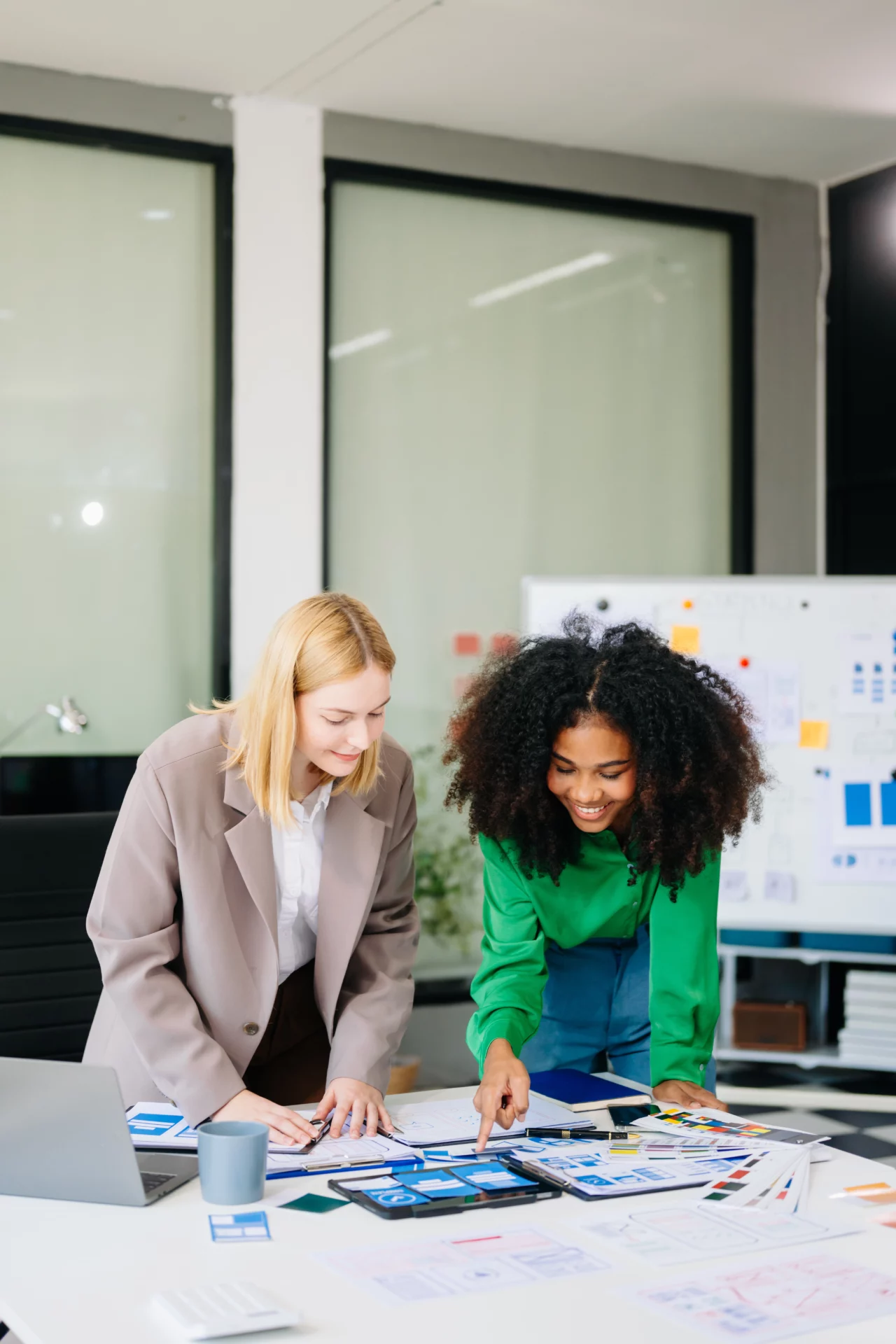 Deux jeunes designers collaborent sur des maquettes UX/UI et des wireframes dans une agence de communication, en analysant des prototypes et moodboards sur une table de travail.